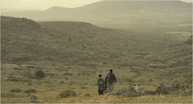 Sur fond de steppe aux couleurs froides, deux jeunes marchent d'un pas décidé avec leur sac à dos.